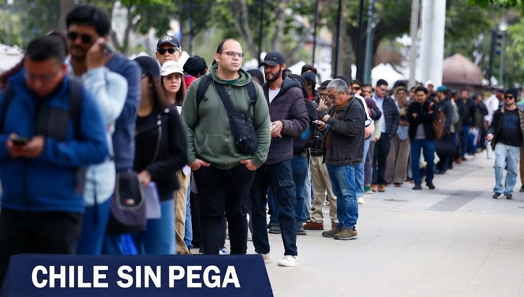 Fila de personas esperando en la vía pública, con un atril agregado que dice «Chile sin pega»