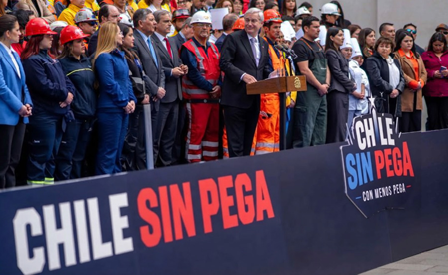 Autoridades y trabajadores en el lanzamiento del plan de empleo; el lienzo del escenario fue alterado para decir «Chile sin pega»