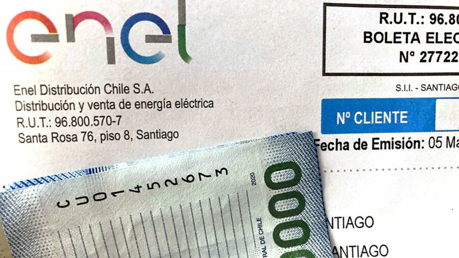 Primer plano de una boleta de electricidad de Enel Distribución Chile junto a un billete