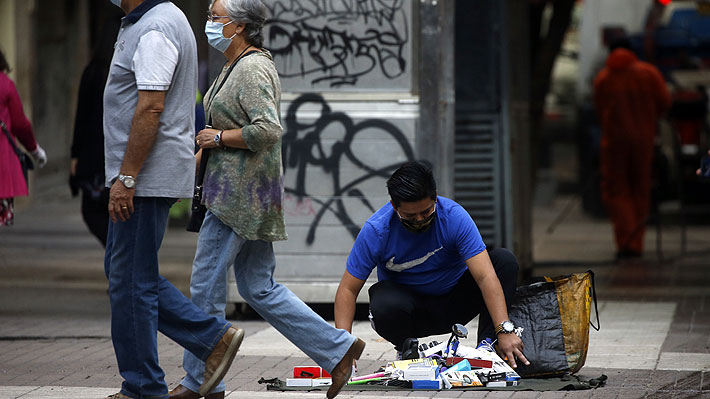 Un comerciante ambulante instala sus productos en la vereda de una calle, mientras pasan peatones